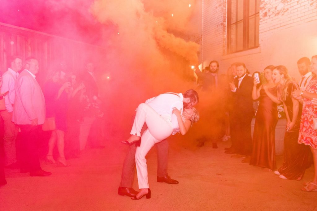 couple exiting reception with smoke bombs and cheering crowd